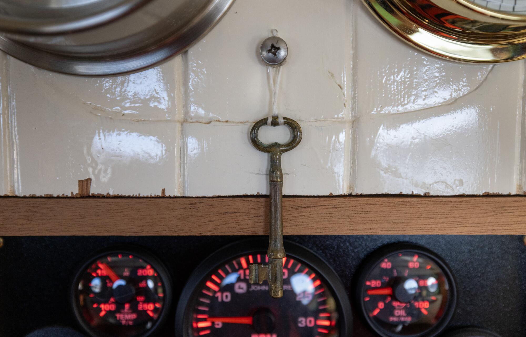 A key hands from a metal screw in a wall above a set of three red-lighted dials.