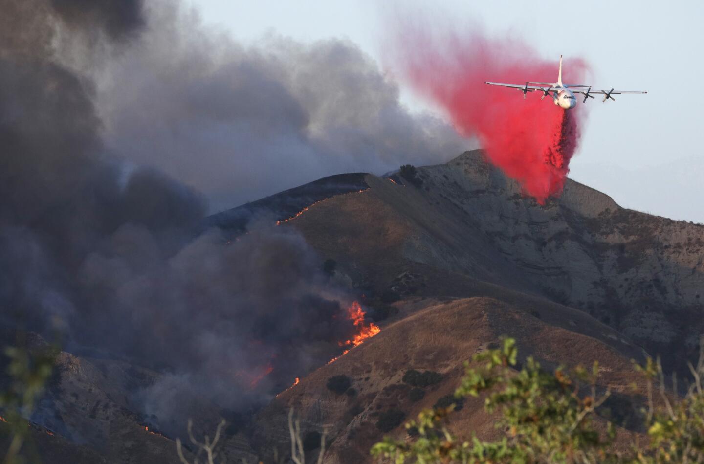 A plane drops fire retardant on a flaming ridge