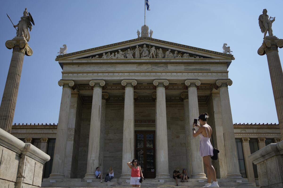 Tourists take photographs and others sit in front of Athens Academy in Athens, Greece, Friday Aug. 19, 2022. Greece's close financial oversight by European Union creditors ends Saturday, closing an unwelcome chapter dating to the painful bailout years.(AP Photo/Thanassis Stavrakis)