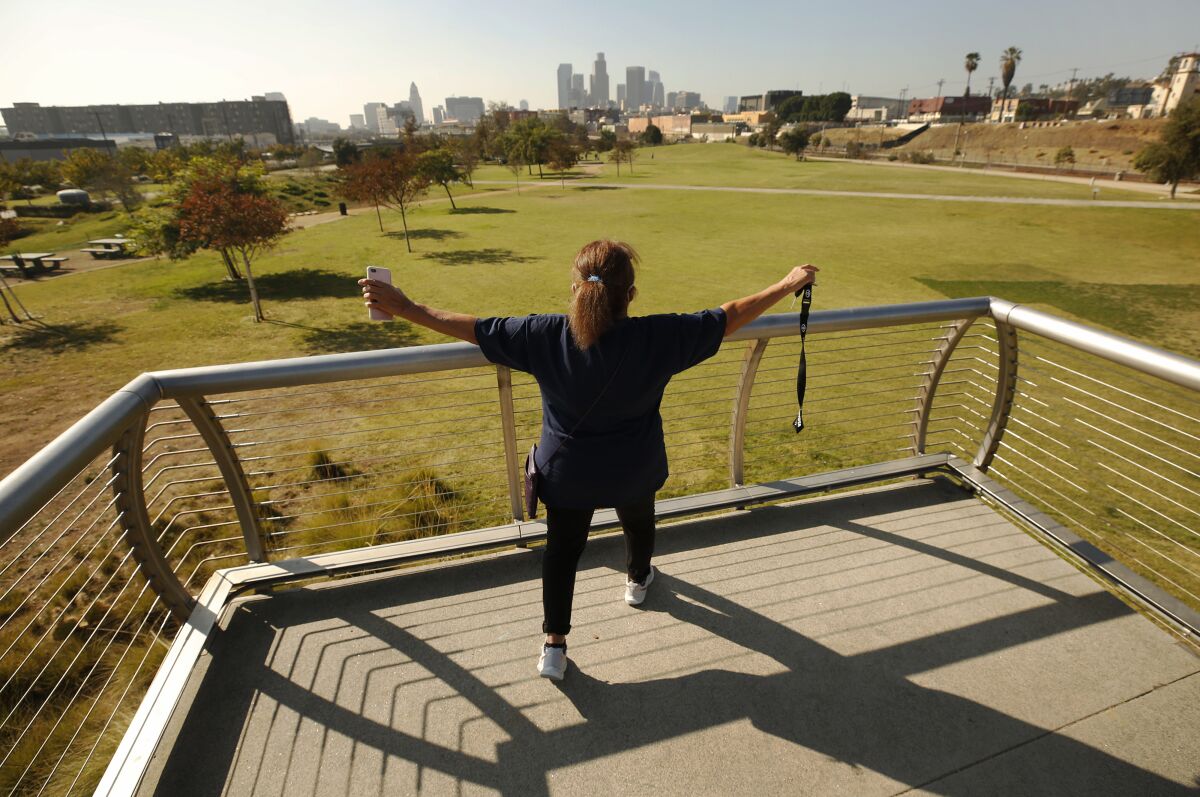 A woman stands on the pedestrian bridge overlooking Los Angeles State Historic Park with her arms outstretched