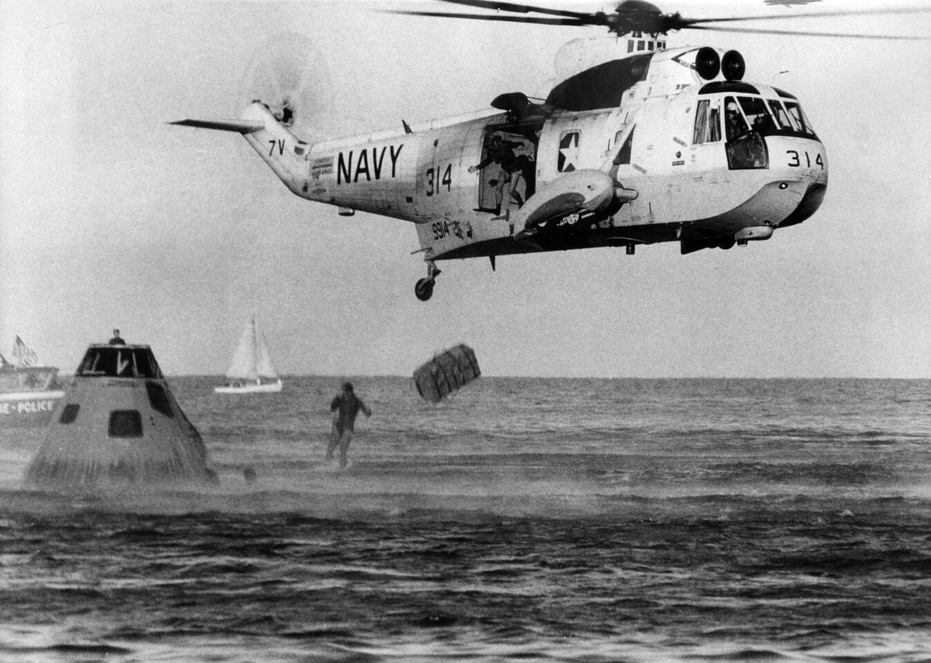 A Navy helicopter flies over a frogman during a simulation in Lake Michigan demonstrating how the frogmen recovered the Apollo 11 astronauts after splashdown in the Pacific Ocean. A replica of the Apollo 11 capsule floats in Lake Michigan as the helicopter makes the pickup on Aug. 22, 1969. The frogman is pulled up to the helicopter to complete the simulation.