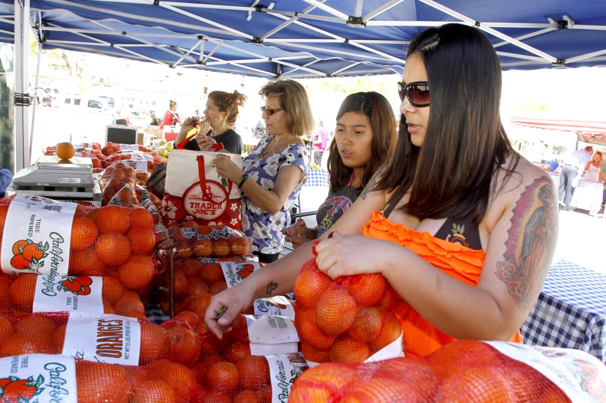 Mia Ruan of Glendale, right, picks up a bag of oranges at the Glendale farmers market at its new location on Thursday, April 24, 2014.