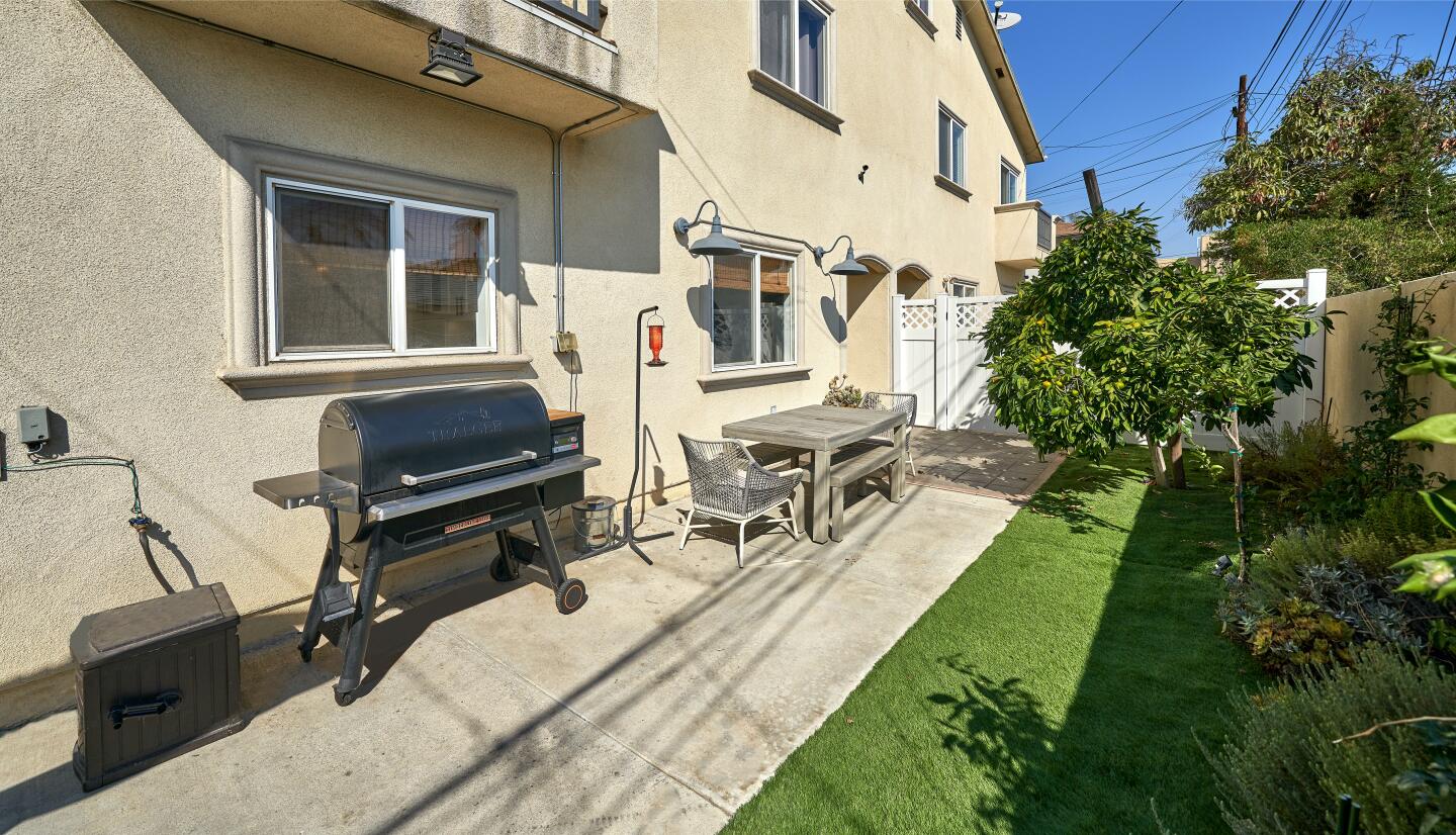 The yard includes a portable grill and a dining set next to the house with grass and trees.