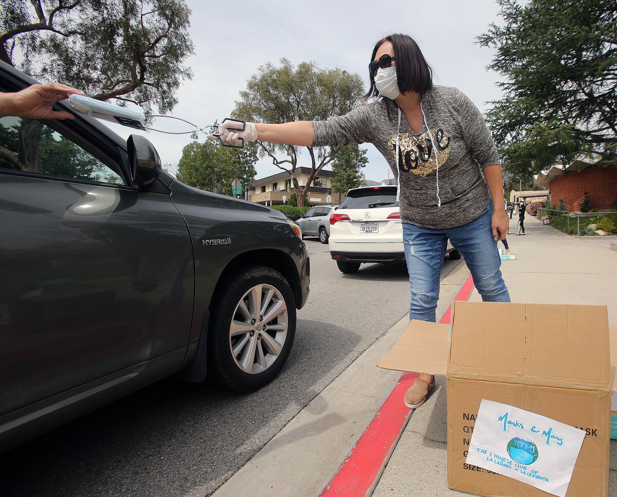 Caroline Anderson uses barbecue tongs to pass out a packet of 10 face masks to a person in their car as part of the Chinese Club of La Cañada Flintridge and La Crescenta's Masks for Many program to help senior citizens in the community protect themselves amid the coronavirus outbreak. 