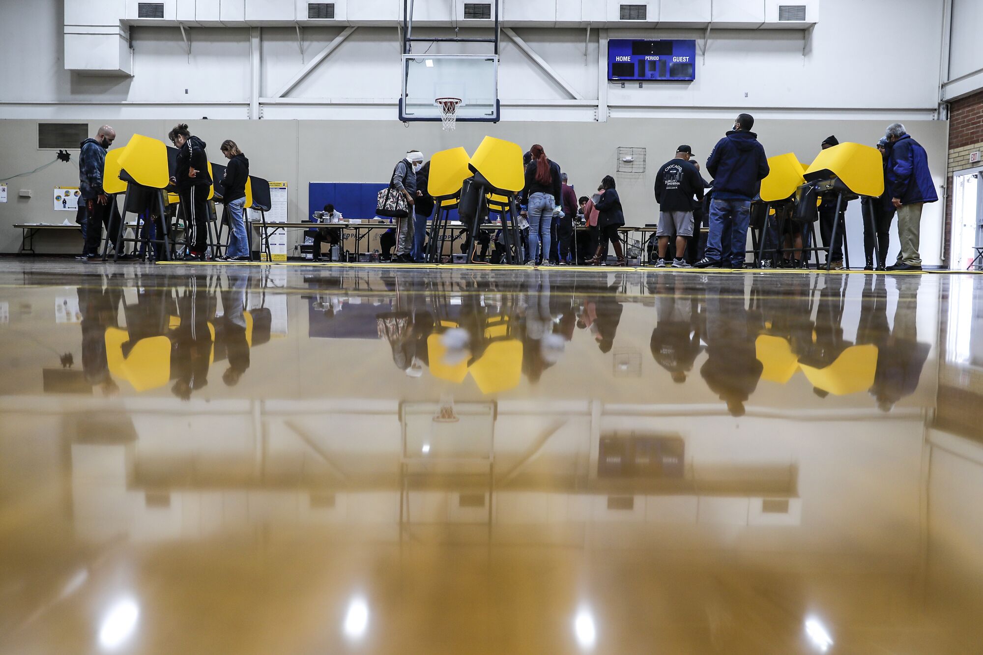 Les gens se tiennent devant des isoloirs jaunes dans un gymnase de basket-ball