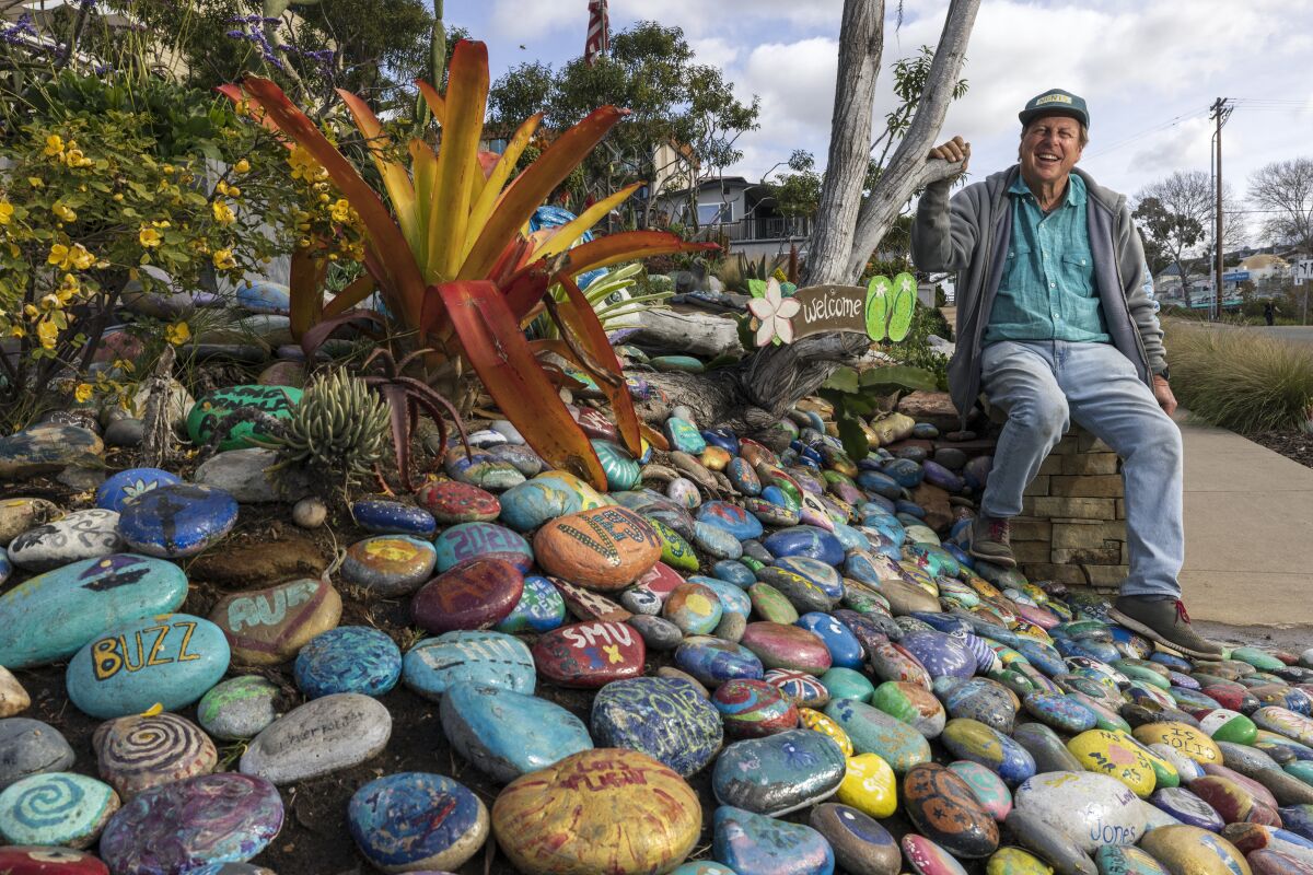 Encinitas resident Dave Dean, 64, sits next to painted rocks at Dave's Rock Garden in Encinitas
