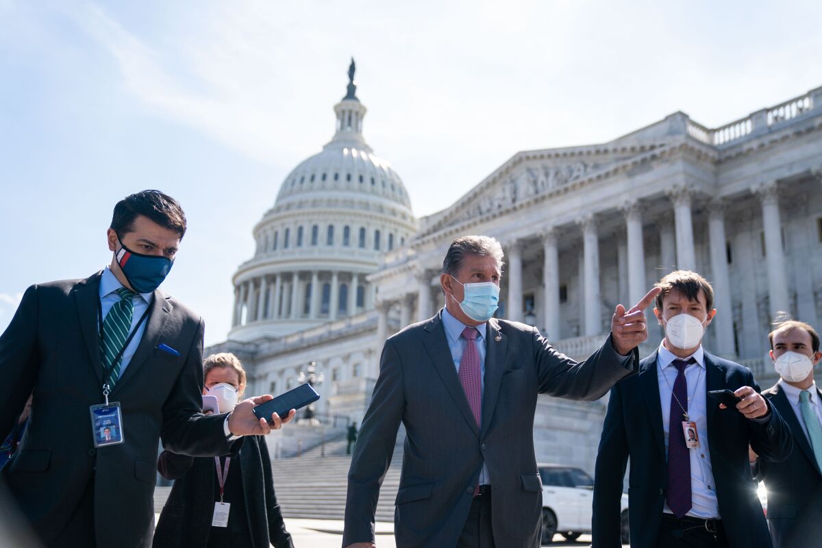 A masked man in a suit and tie, flanked by other men, also in masks and suits, gestures outside the U.S. Capitol 