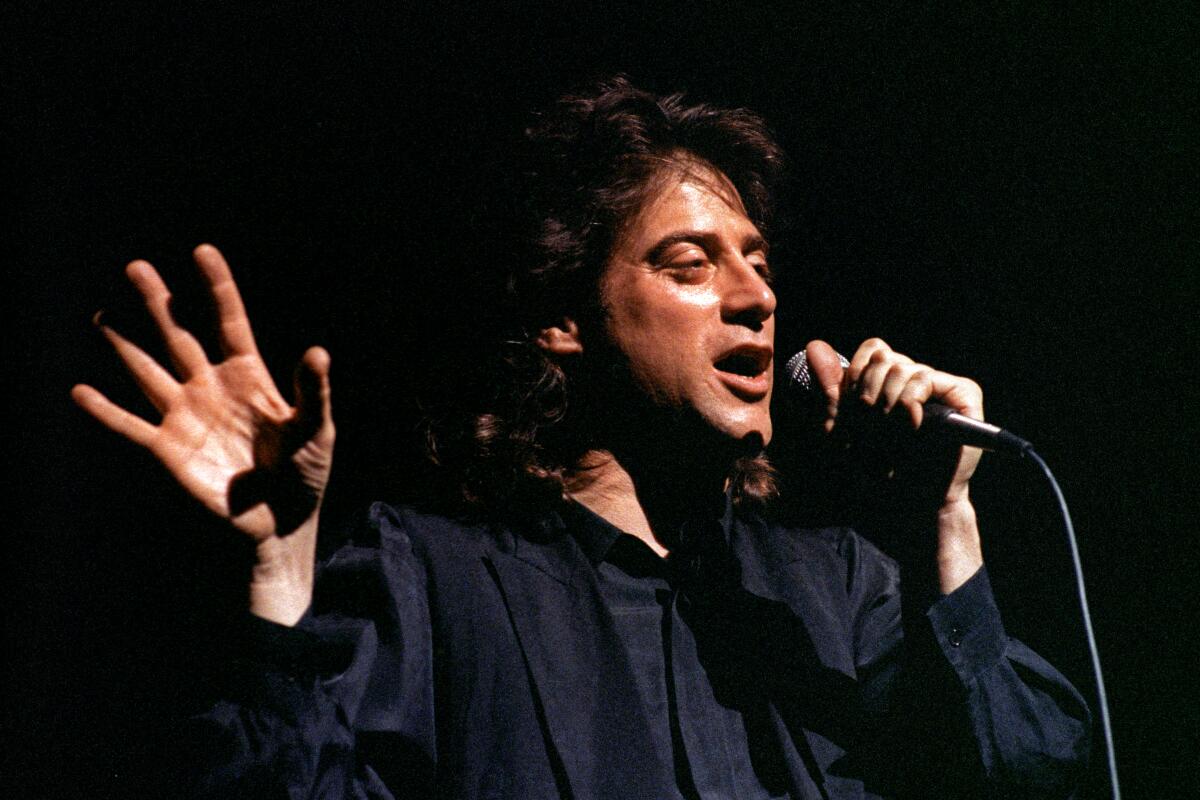Richard Lewis, wearing black against a black background, performs stand-up.
