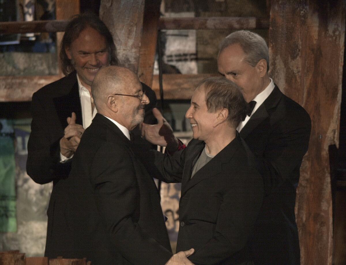 FILE - Record executive Mo Ostin, foreground left, is embraced by singer/songwriter Paul Simon, right, as singer/songwriter Neil Young, background left, and producer Lorne Michaels look on after Ostin was inducted into the Rock and Roll Hall of Fame in New York on March 10, 2003. Ostin, a self-effacing giant of the music business who with rare integrity presided over Warner Bros. Records’ rise to a sprawling, billion-dollar empire, died Sunday, July 31, 2022. He was 95. (AP Photo/Gregory Bull, File)