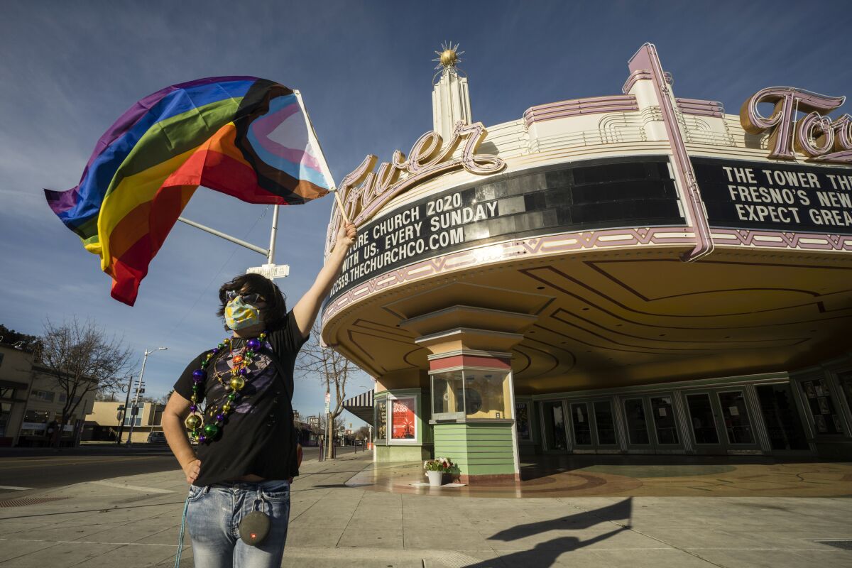 A person holds a rainbow flag in front of a theater