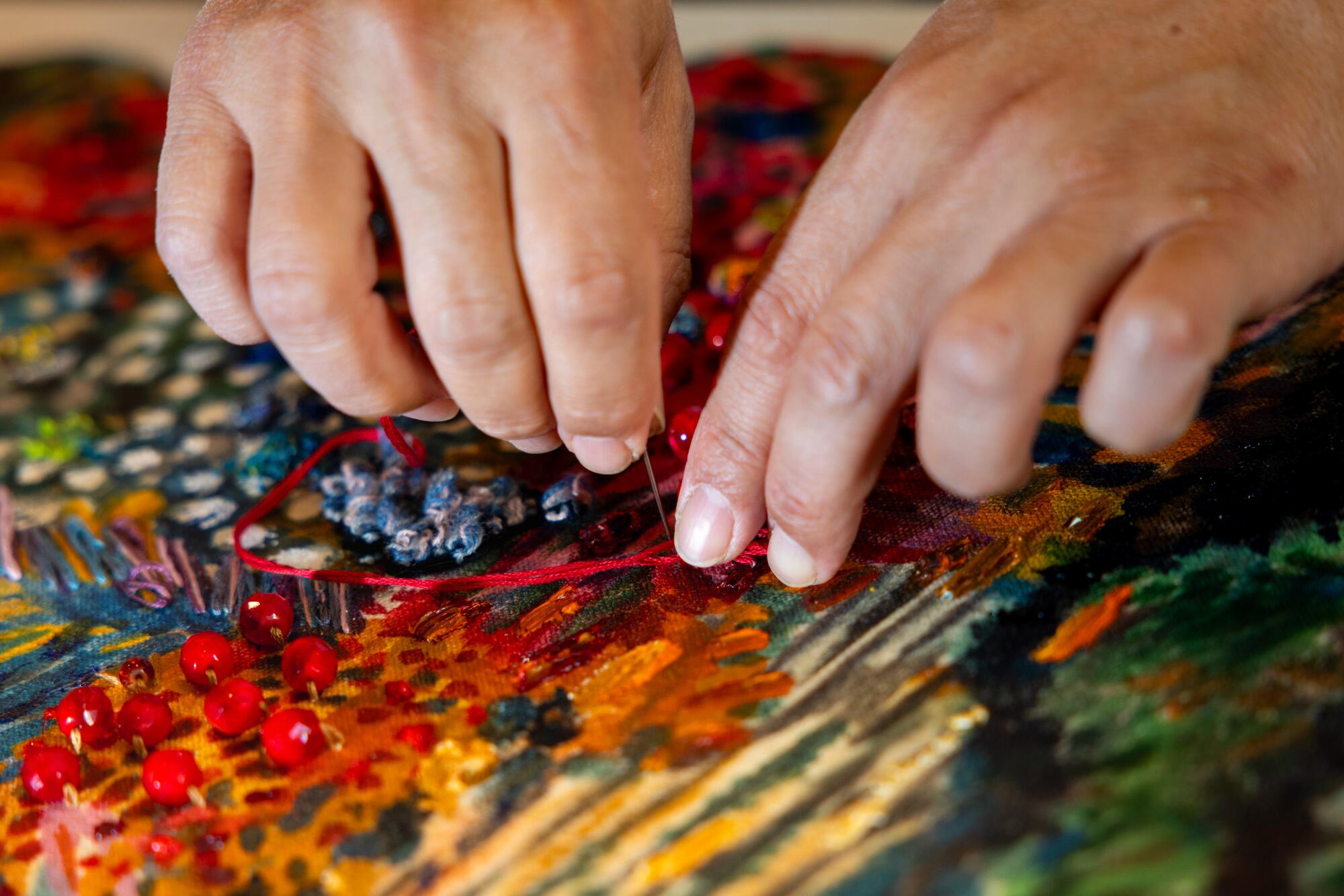 Ken Gun Min sews red beads onto his canvas 