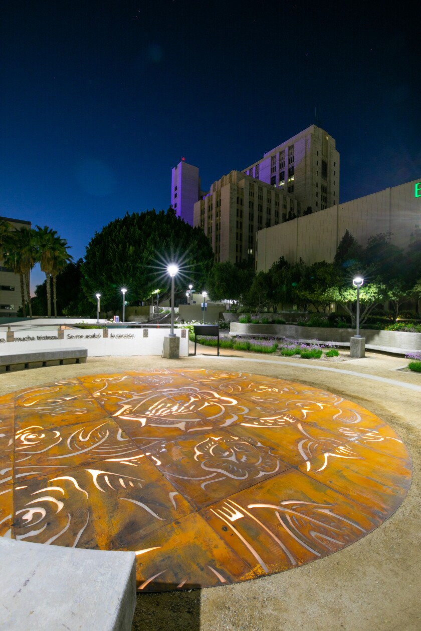 A circular work of art in tiles on a concrete plaza at dusk.