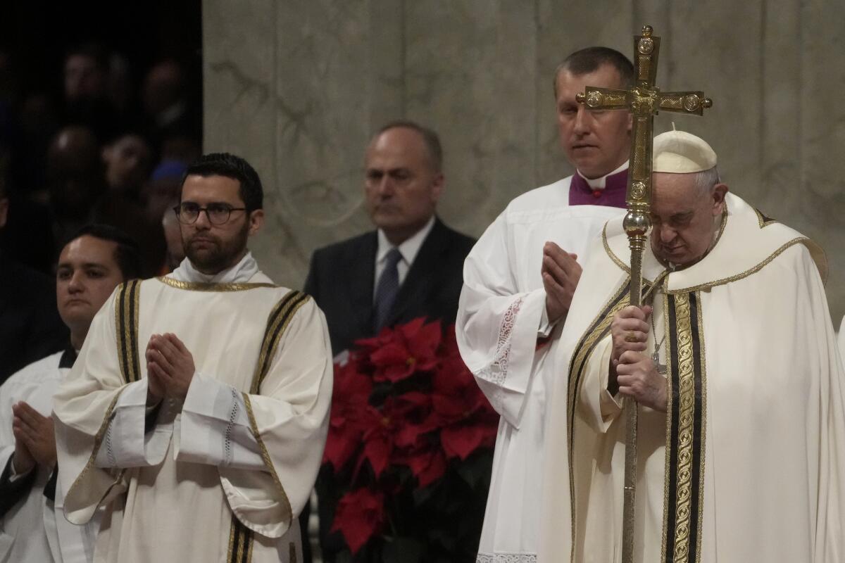 Pope Francis holds his pastoral staff as he presides over Christmas Eve Mass while others stand nearby.