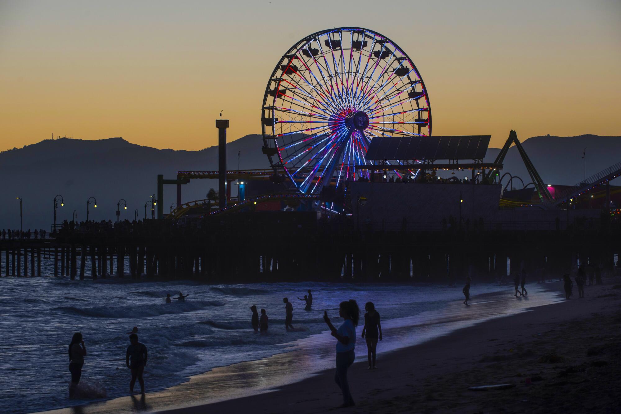 People on the beach and in the water near a Ferris wheel and pier