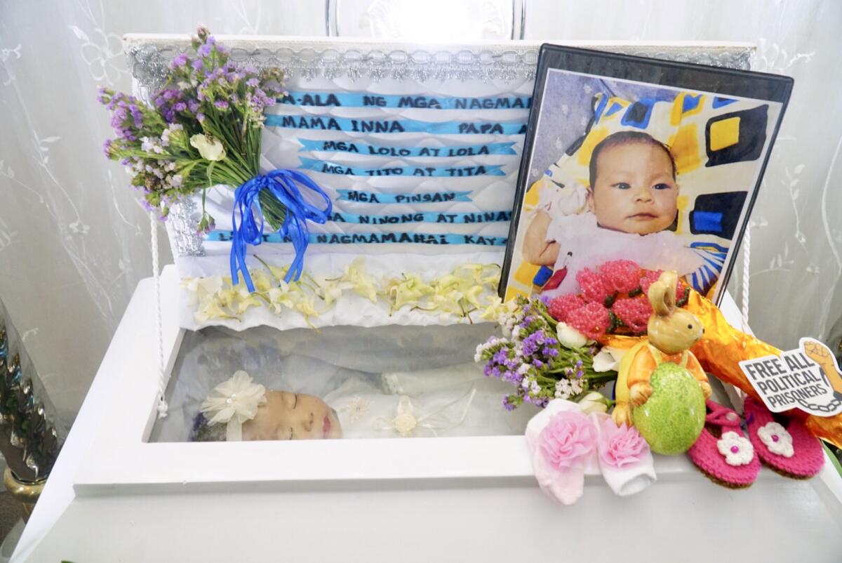 Reina Mae Nasino's baby, River, lies in a white casket adorned with her photo, flowers, baby shoes and a ceramic bunny.