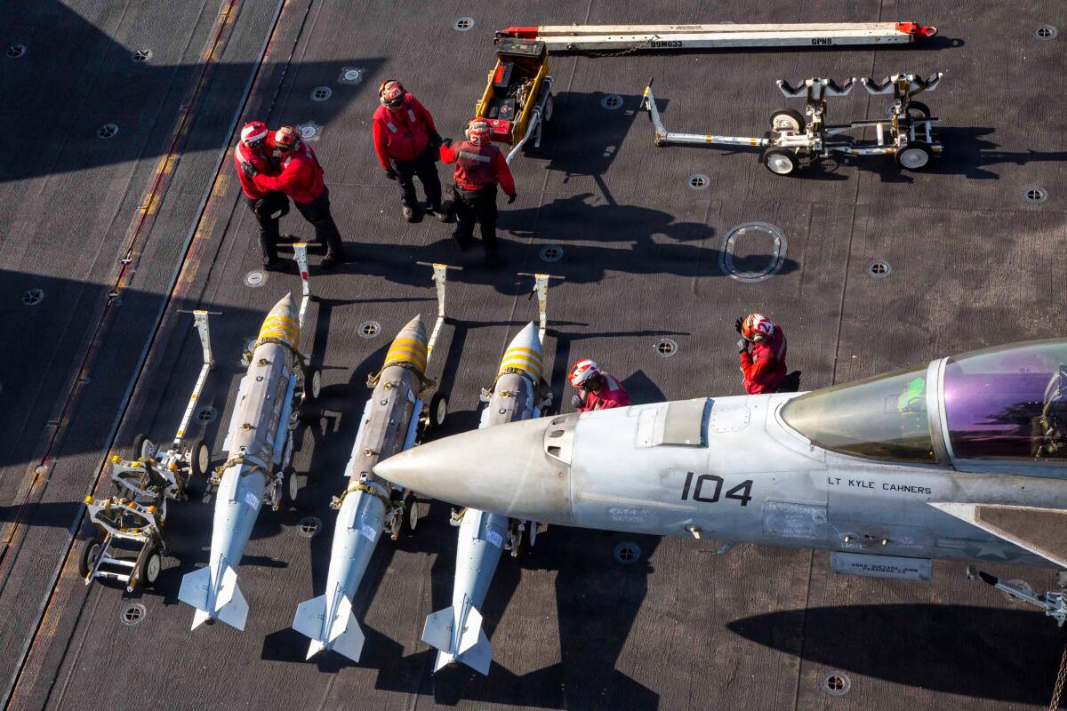 Sailors stand with ordnance next to an F/A-18F Super Hornet on a ship's deck
