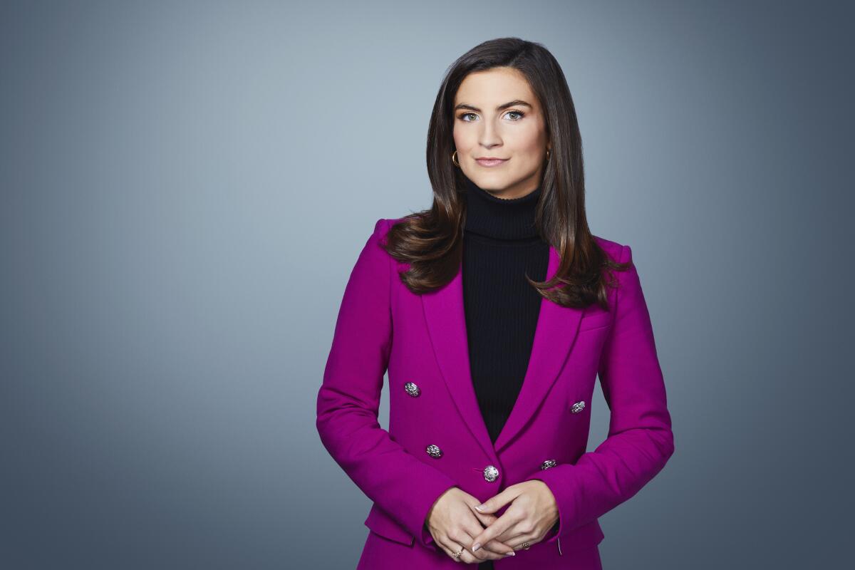 A dark-haired woman in a black top and purple jacket.