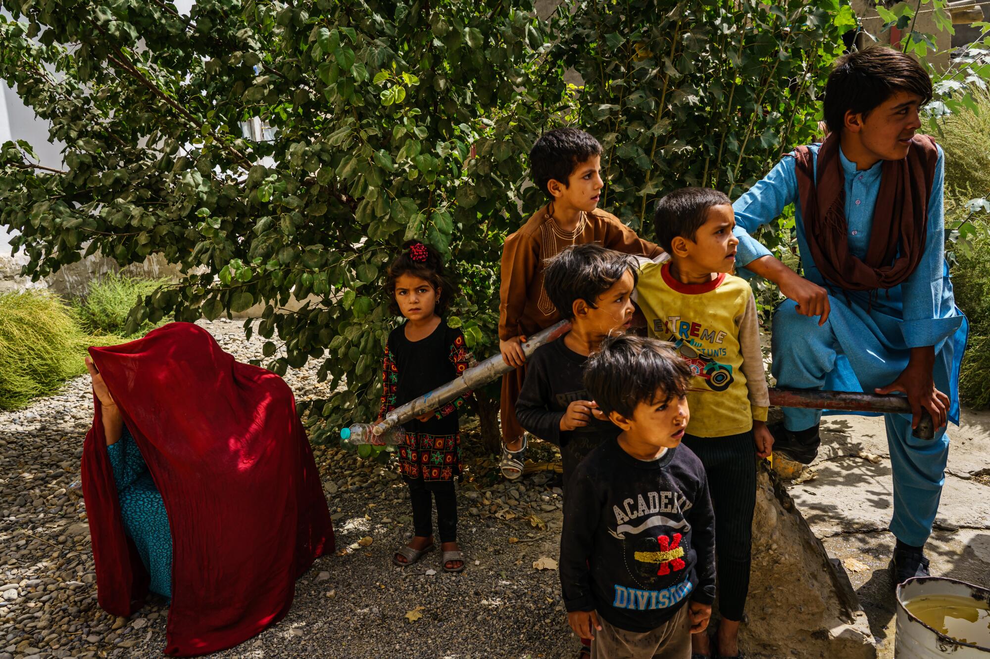 A person crouches, covered by a large piece of fabric; children stand nearby.