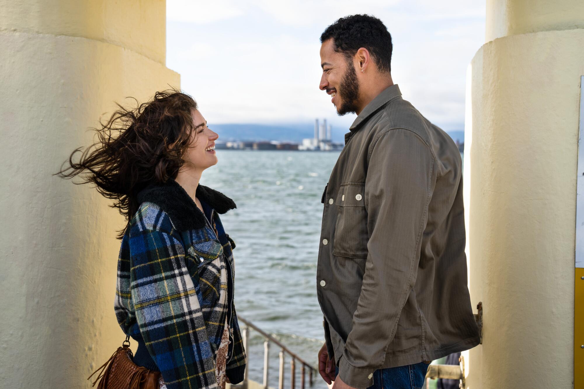 A couple standing by the seashore smiling at each other.