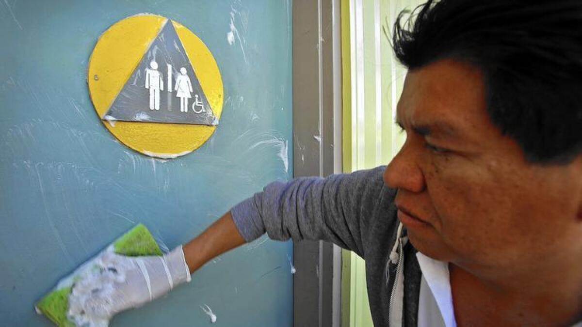 Edgar Lopez, a maintenance worker with the city of West Hollywood, cleans the front door of a restroom at Plummer Park.