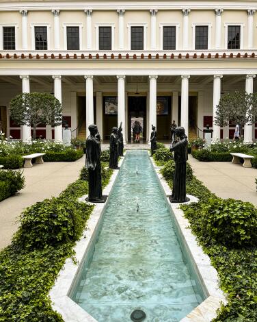 A reflecting pool lined with statues in the garden in front of a classical-style building