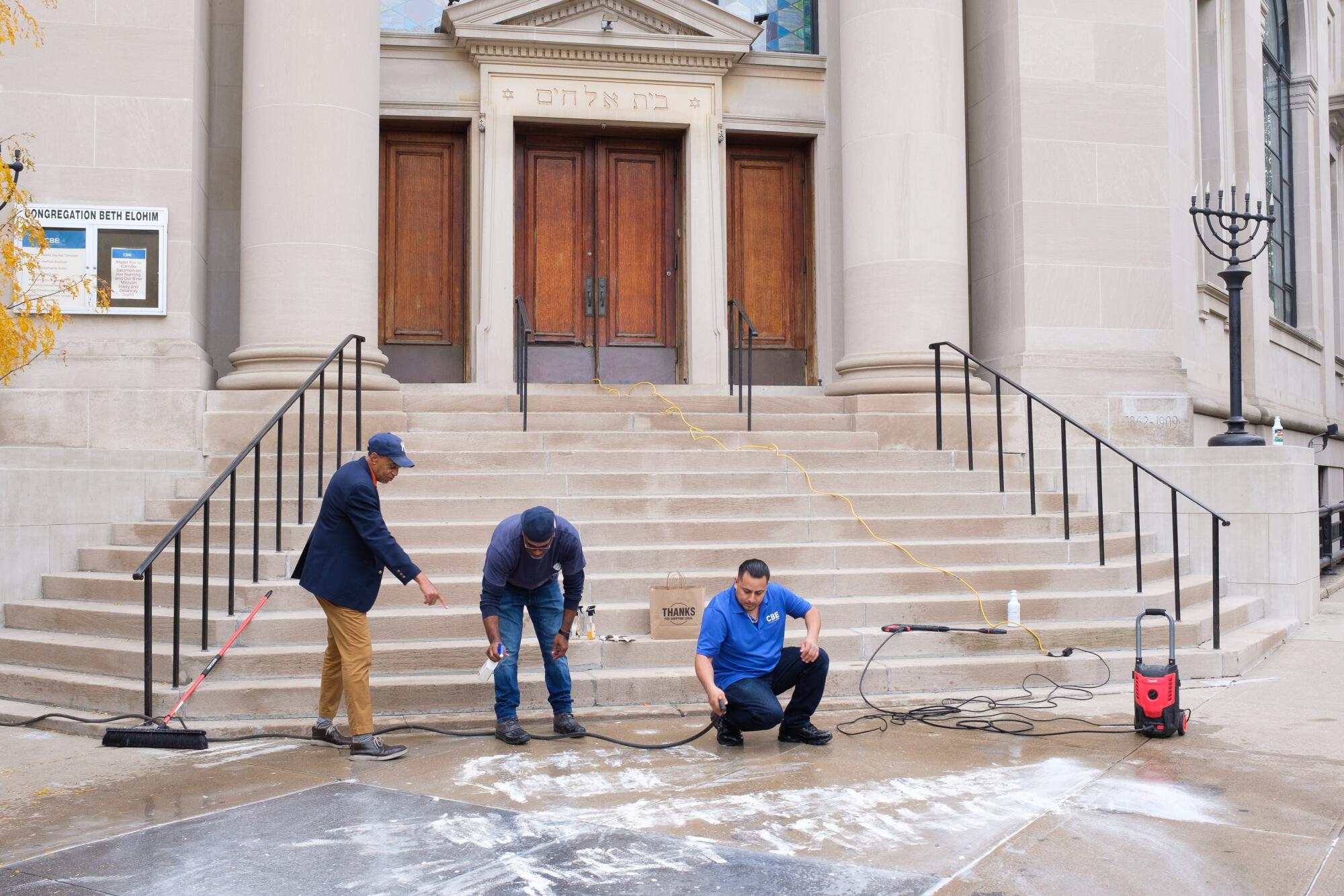 Workers clean graffiti from a sidewalk outside a synagogue 