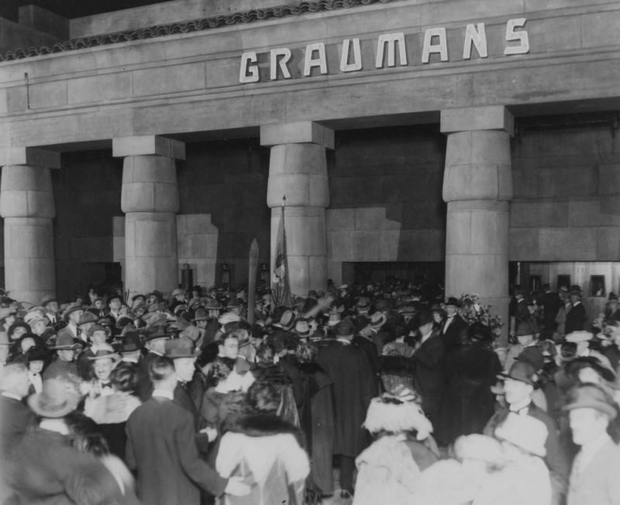 A crowd gathers in the forecourt of a movie palace.