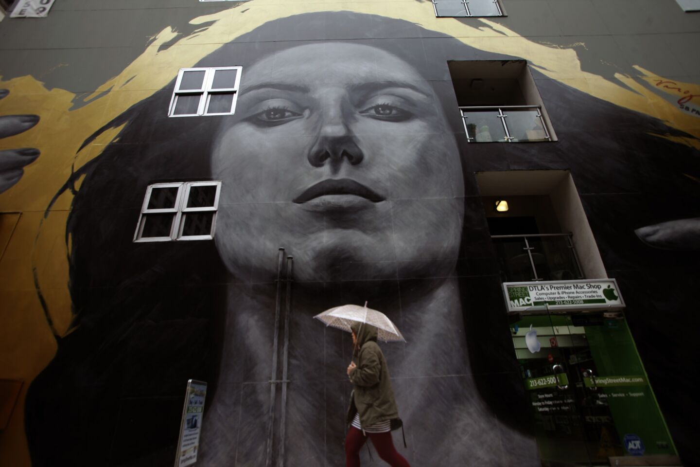 A pedestrian makes her way through the rain past the mural by Robert Vargas and Michael Blaze titled "Our Lady of DTLA," that graces the SB Tower at 6th and Spring streets in downtown Los Angeles in 2014.