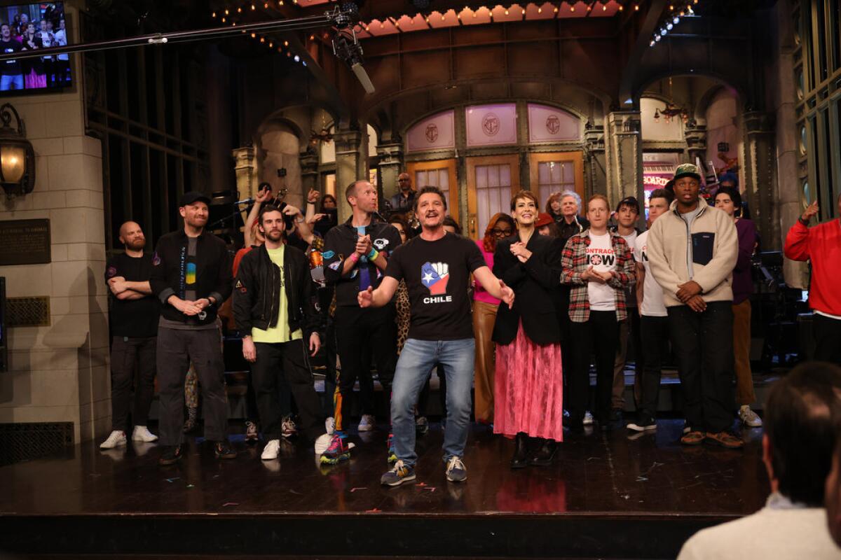 A large group of people stand on a stage in a TV studio.