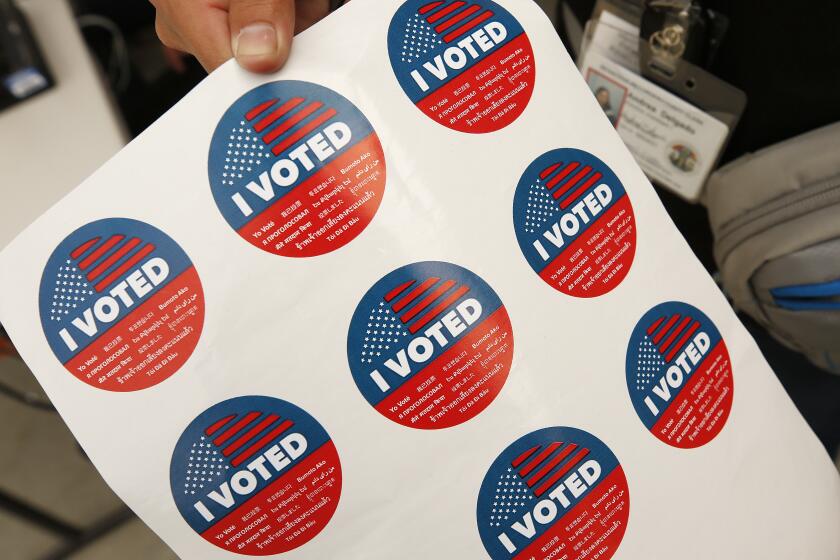 LOS ANGELES, CA - FEBRUARY 27, 2020 Election assistant Andrea Delgado holds stickers at the Mobile Vote Center assembled in Grand Park as the Los Angeles County Registrar-Recorder/County Clerk is trying to provide voters who live and work in downtown with the opportunity to vote in-person in the 12-acre park through 6 p.m. on Thursday. This is part of the county's transition from polling places to vote centers as residents are able to vote at any vote center and are no longer assigned to a specific polling location for in-person voting. (Al Seib / Los Angeles Times)