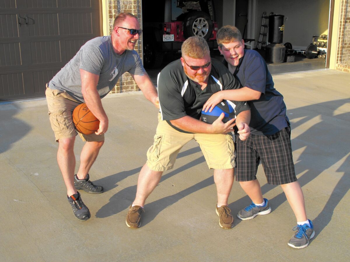 Brett Jones, left, the first openly gay Navy SEAL, plays basketball with his husband, Jason White, and their son, Ethan, 13, outside their Alabama home.