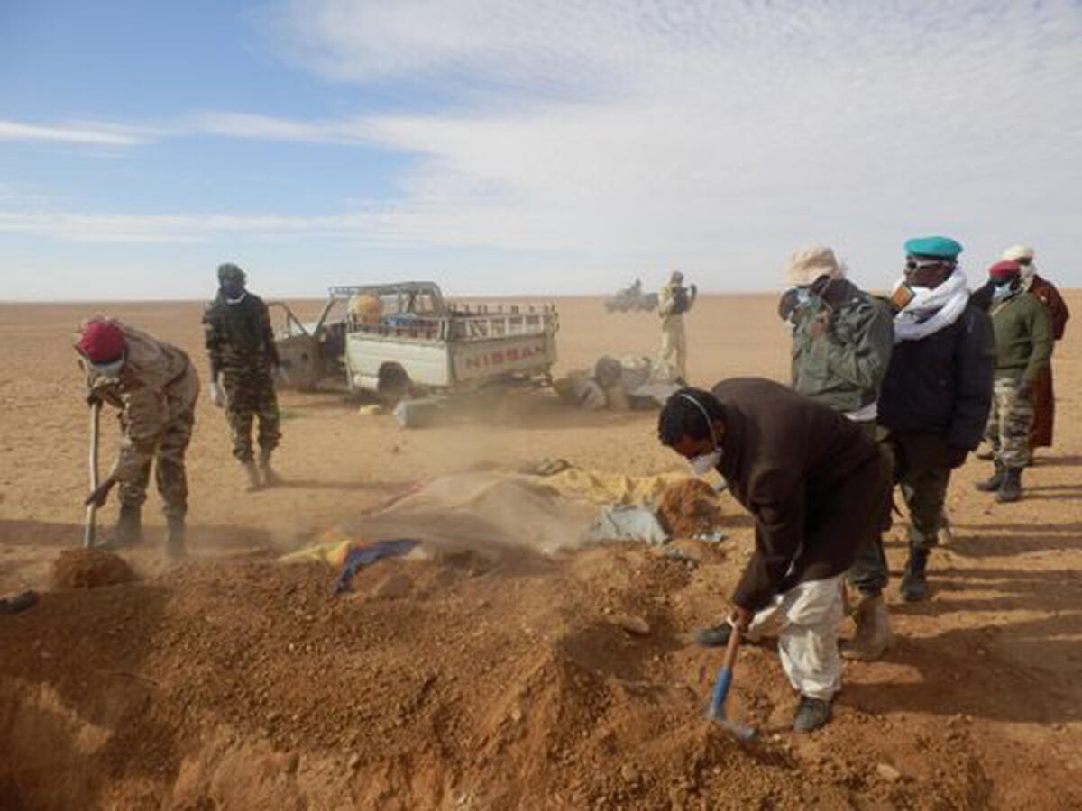 Volunteers and officials dig graves Wednesday to inter the bodies of migrants who died after the truck they were traveling in, seen in the rear rear, broke down while attempting to cross the Sahara Desert north of Arlit, Niger.
