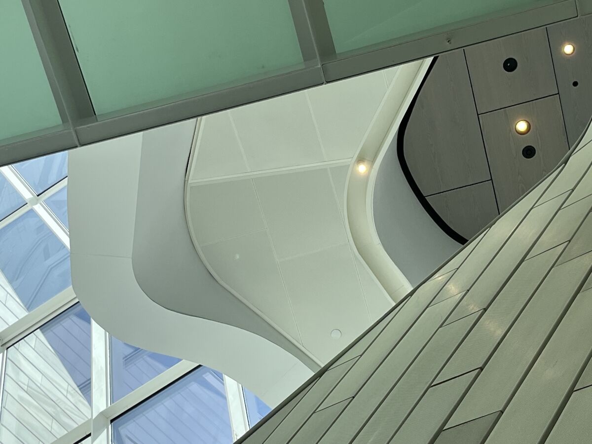 An upward view of an atrium reveals some sky as well as undulating ceiling panels framed by imperfectly installed trim.