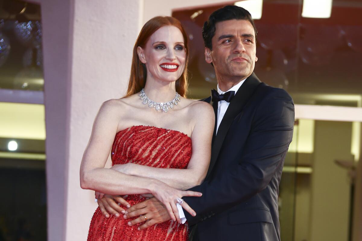 Oscar Isaac holds Jessica Chastain around her waist as the two smile and pose on a formal red carpet