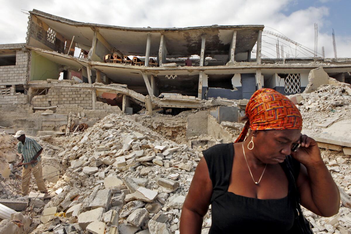 a woman stands among debris from a collapsed building 