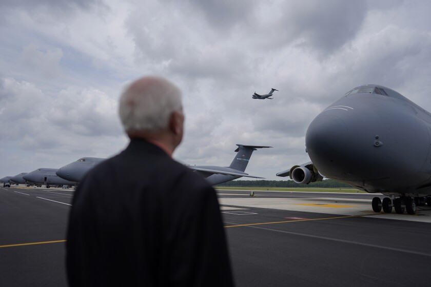 A military chaplain stands in front of a transport plane.
