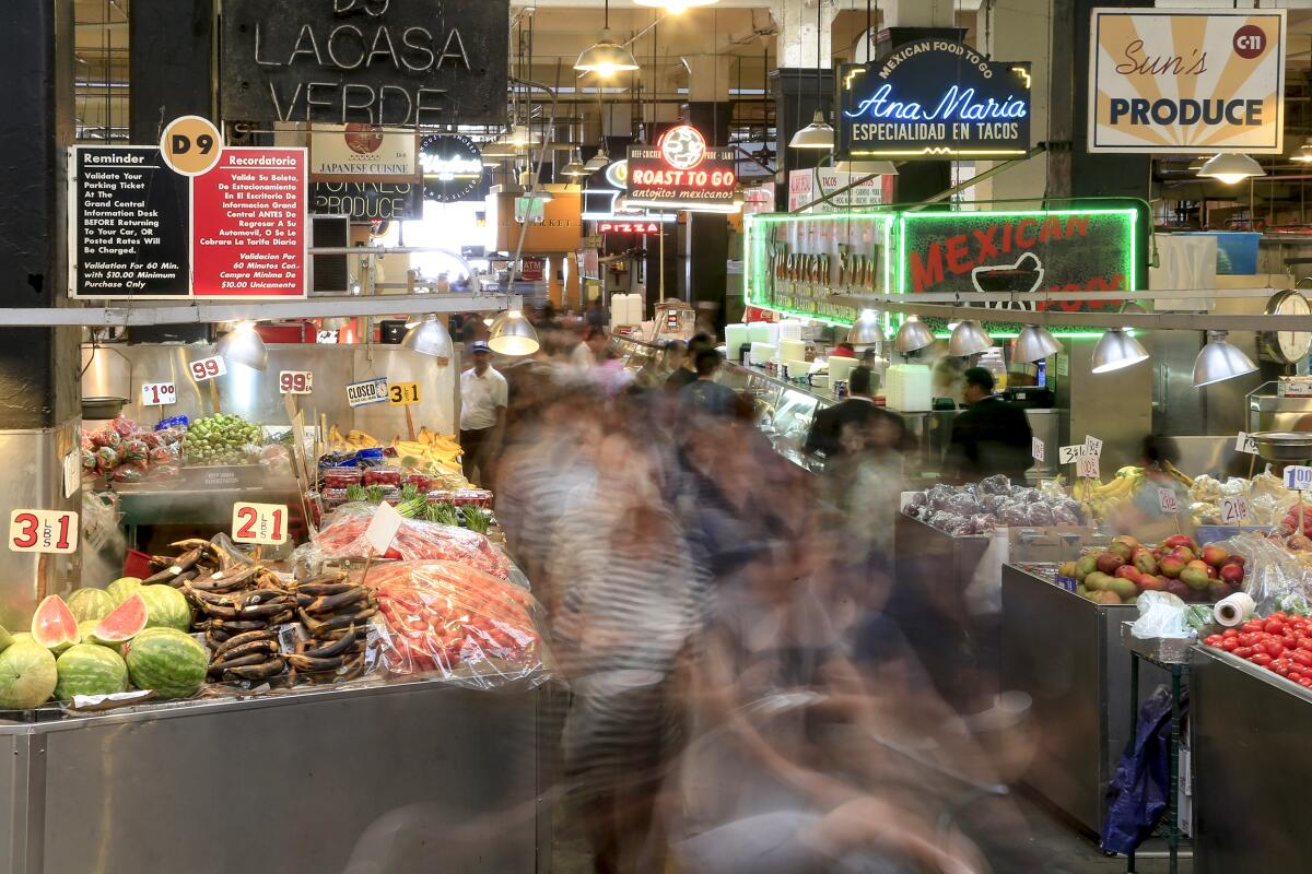 Long-exposure photo of people walking among food and fruit stalls at Grand Central Market