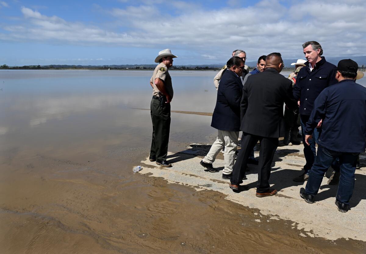 A group of men stand next to an expanse of flood water.