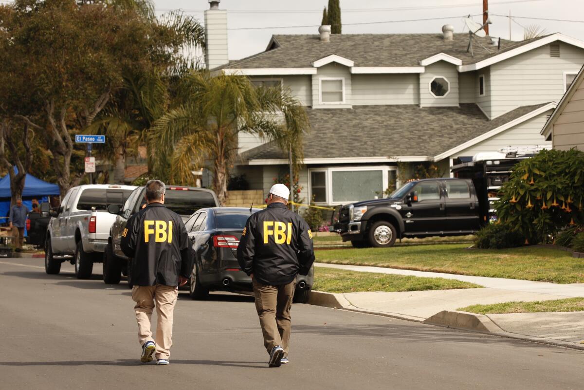 Two men in jackets that say "FBI" walk down a residential street.