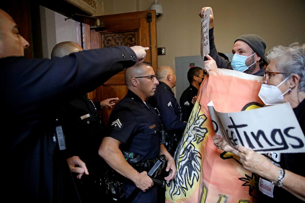 Police officers and people in masks holding signs face one another inside a city building.