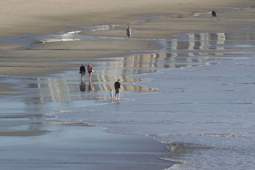 Beach-goers walk in the wet sand exposed at the lowest point in the latest king tides near Pacific Edge hotel in Laguna Beach on Sunday.