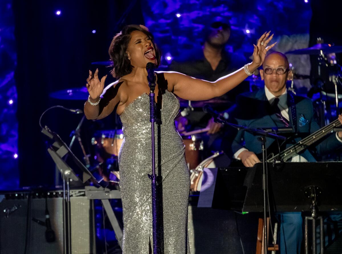 A female singer in a silver gown performs onstage