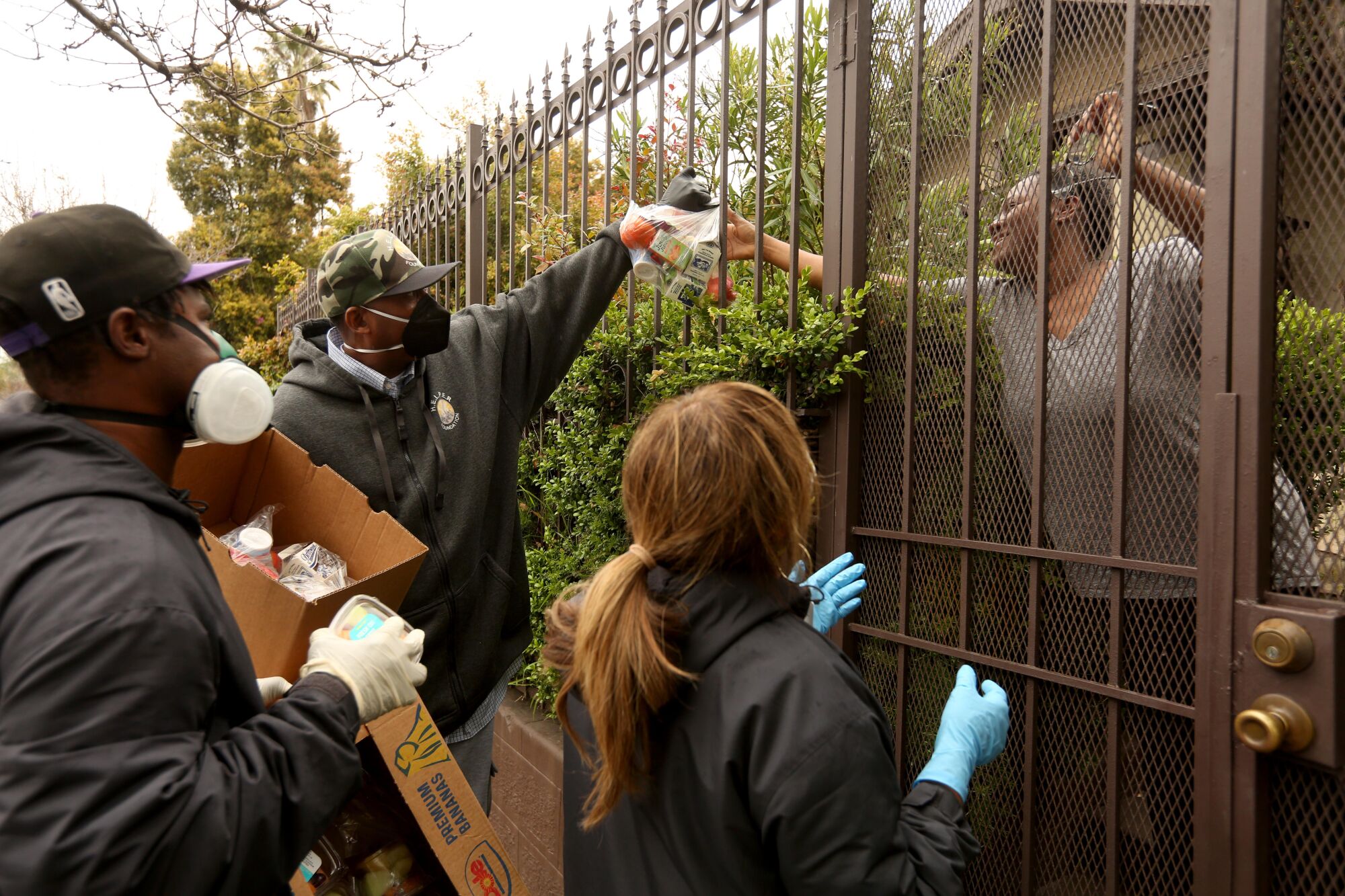 Ansar “Stan” Muhammad, center, executive director of H.E.L.P.E.R. Foundation, delivers food through a fence to the needy in the Oaklwood Neighborhood of Venice on April 9, 2020. Members with H.E.L.P.E.R. Foundation deliver food and groceries to the needy, those who have lost their jobs and seniors who are sheltering in place in the neighborhood due to the COVID-19 pandemic.