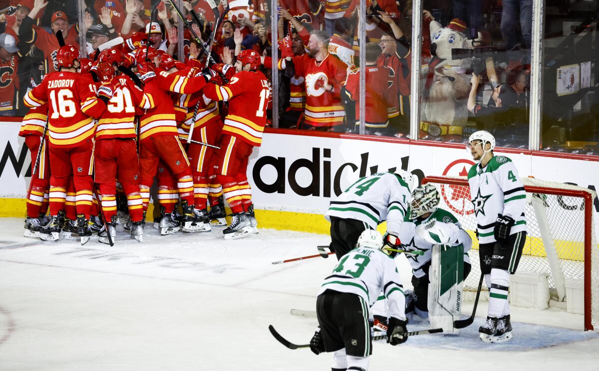 Dallas Stars goalie Jake Oettinger, second from right, is consoled by teammates as Calgary Flames celebrate following overtime NHL playoff hockey action in Calgary, Alberta, Sunday, May 15, 2022. (Jeff McIntosh/The Canadian Press via AP)