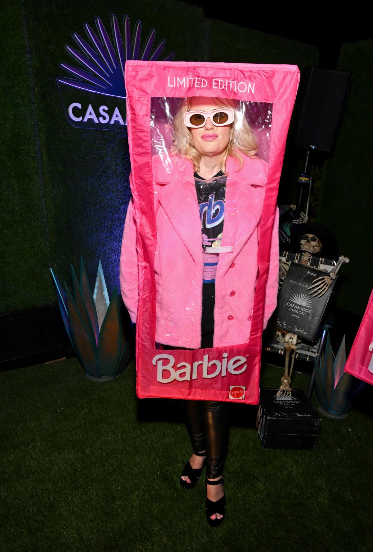 A blond woman with sunglasses posing in a giant fake Barbie box