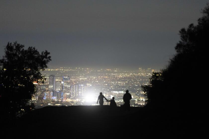 A family is silhouetted against the city lights while walking along a trail at the Griffith Park in Los Angeles, Monday, Nov. 14, 2022. The world's population is projected to hit an estimated 8 billion people on Tuesday, Nov. 15, according to a United Nations projection. (AP Photo/Jae C. Hong)