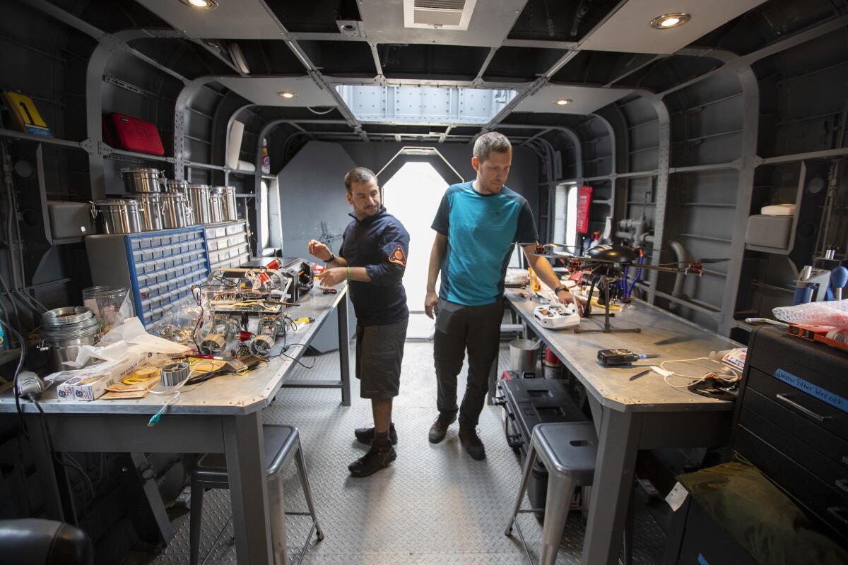 Italian engineers Vittorio Netti, left, and Paolo Guardabasso, right, assemble drones to test the technology, operations, and science required for human space exploration of Mars inside the repair and assembly module, a retrofitted Chinook helicopter at the Mars Desert Research Station near Hanksville, Utah. (Brian van der Brug / Los Angeles Times)
