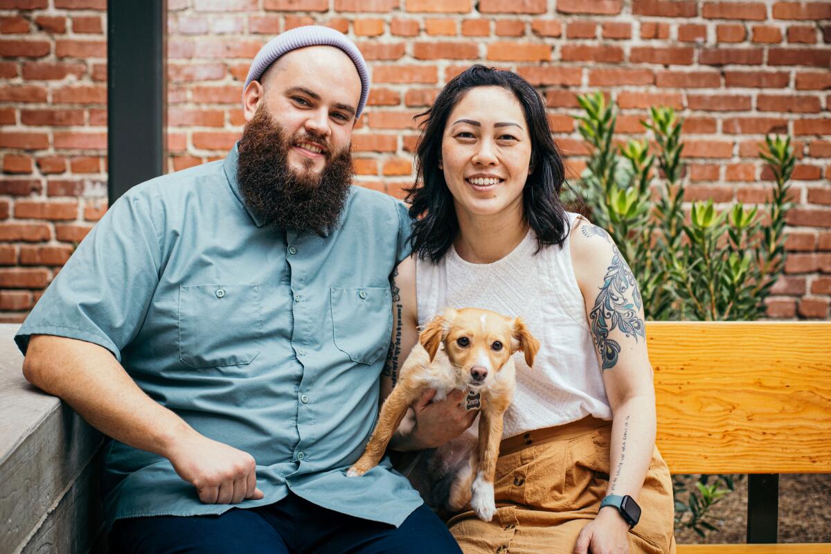 A man sits on a bench next to a woman holding a small dog.