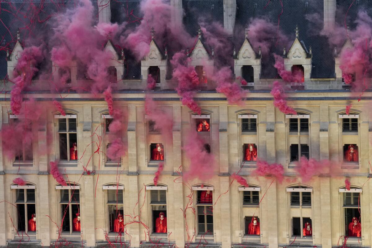 Pink smoke billowing from windows as performers in red stand in the openings. 