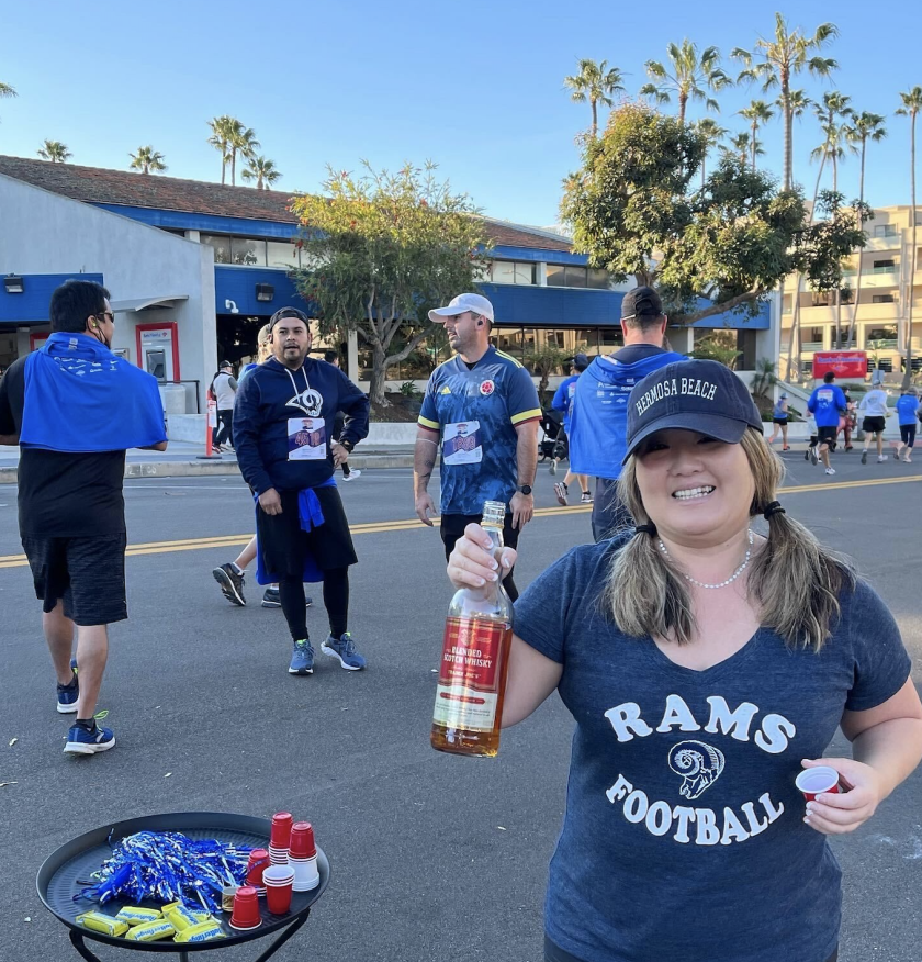 A woman in a Rams Football T-shirt holds up a bottle of liquor.